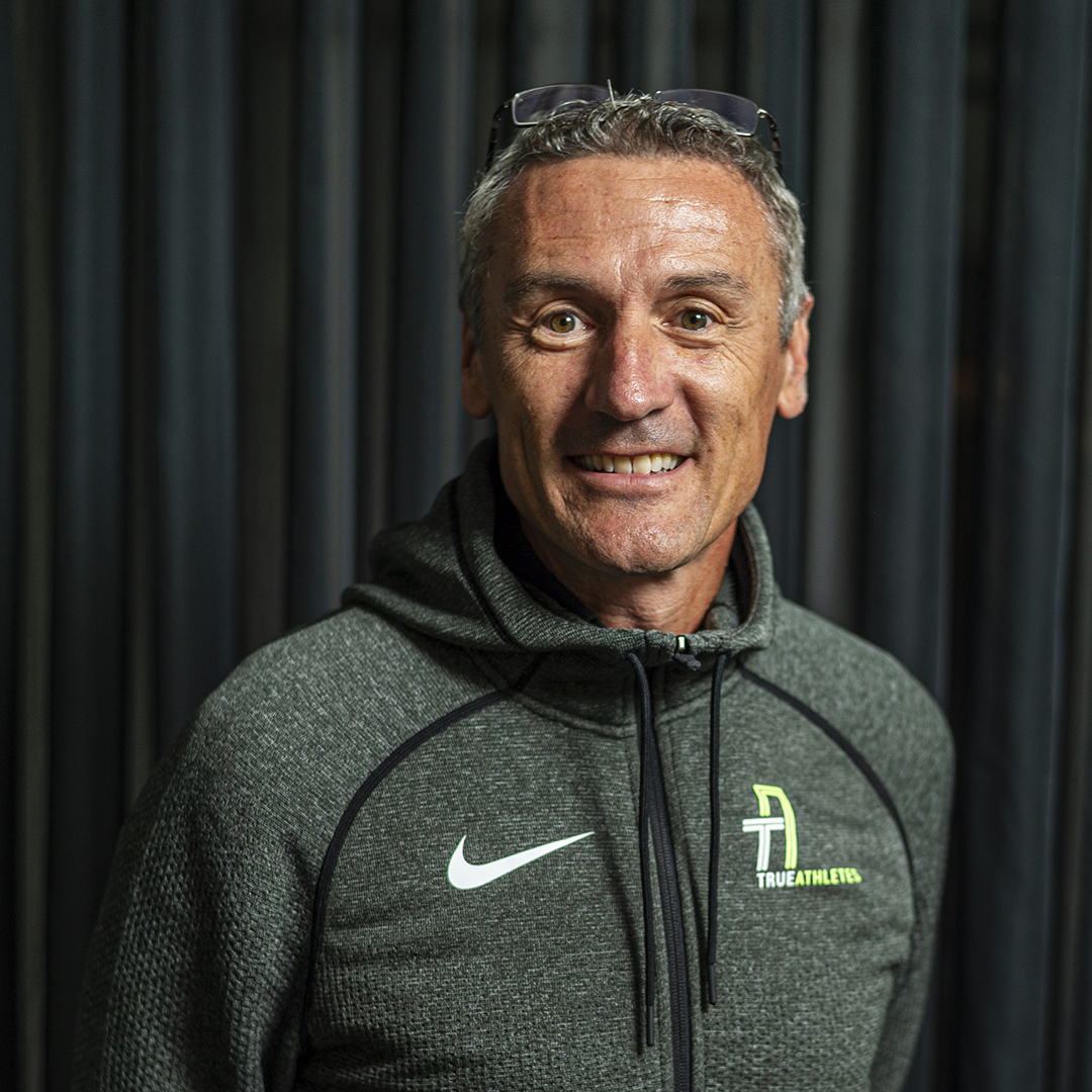 Porträt von Dominic Ullrich mit grauen Haaren trägt einen grauen Sportpullover mit einem Nike-Logo. Er steht vor einem neutralen Hintergrund und hat eine sportliche Ausstrahlung.