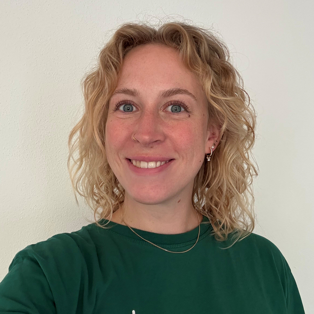 Porträt von Lena Müller mit lockigem, blondem Haar trägt ein grünes T-Shirt. Der Hintergrund ist hell und neutral. 