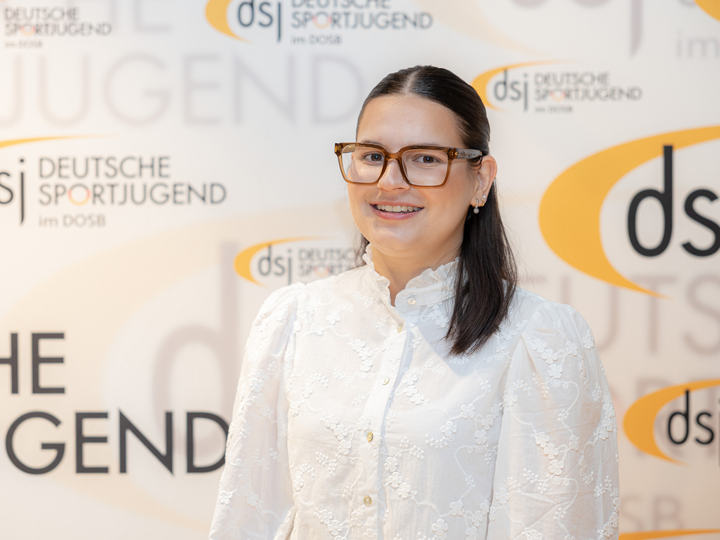 Porträt von Leandra Giannaki vor einer dsj-Logowand.