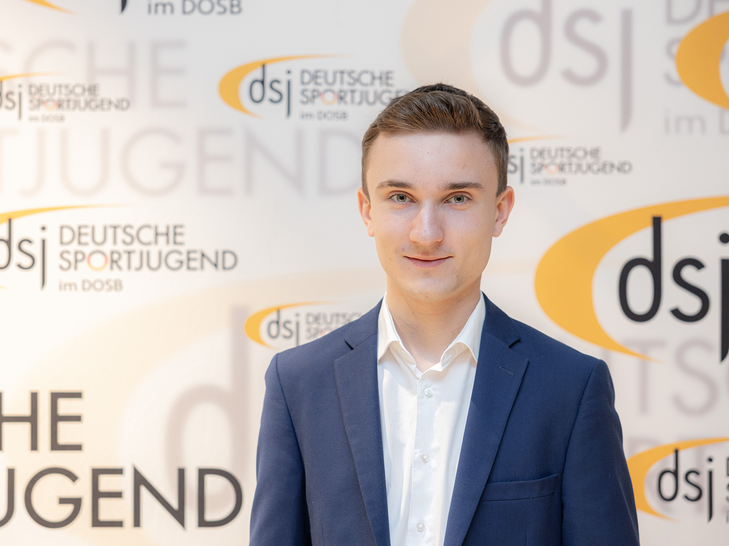 Porträt von Tom Faßhauer vor einer dsj-Logowand.