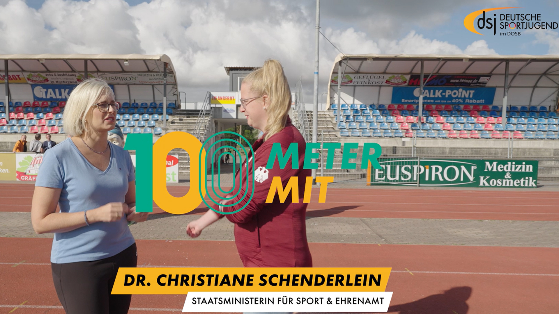 Dr. Christiane Schenderlein, Staatsministerin für Sport und Ehrenamt, steht auf der Tartanbahn des Ilburg Stadions in Eilenburg. Carolin Giffhorn, Vorstandsmitglied der dsj, spricht mit ihr. Im Hintergrund sind Tribünen und Werbebanner sichtbar.