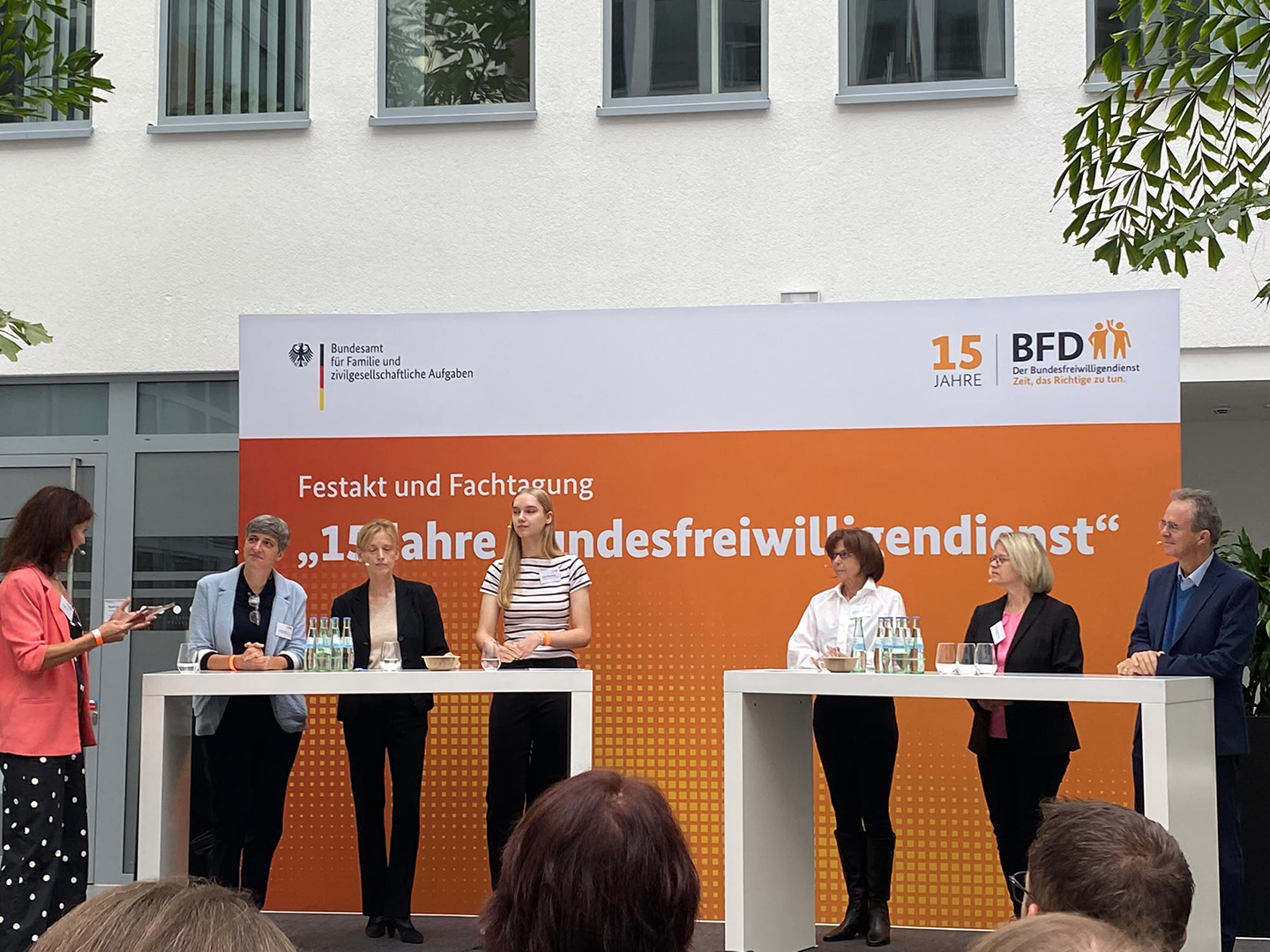 Eine Veranstaltung mit mehreren Personen an Stehtischen, die auf einer Bühne stehen. Im Hintergrund ein Banner mit dem Text „15 Jahre BFD“ und „Festakt und Fachtagung“. Die Anwesenden diskutieren, während eine Person spricht.
