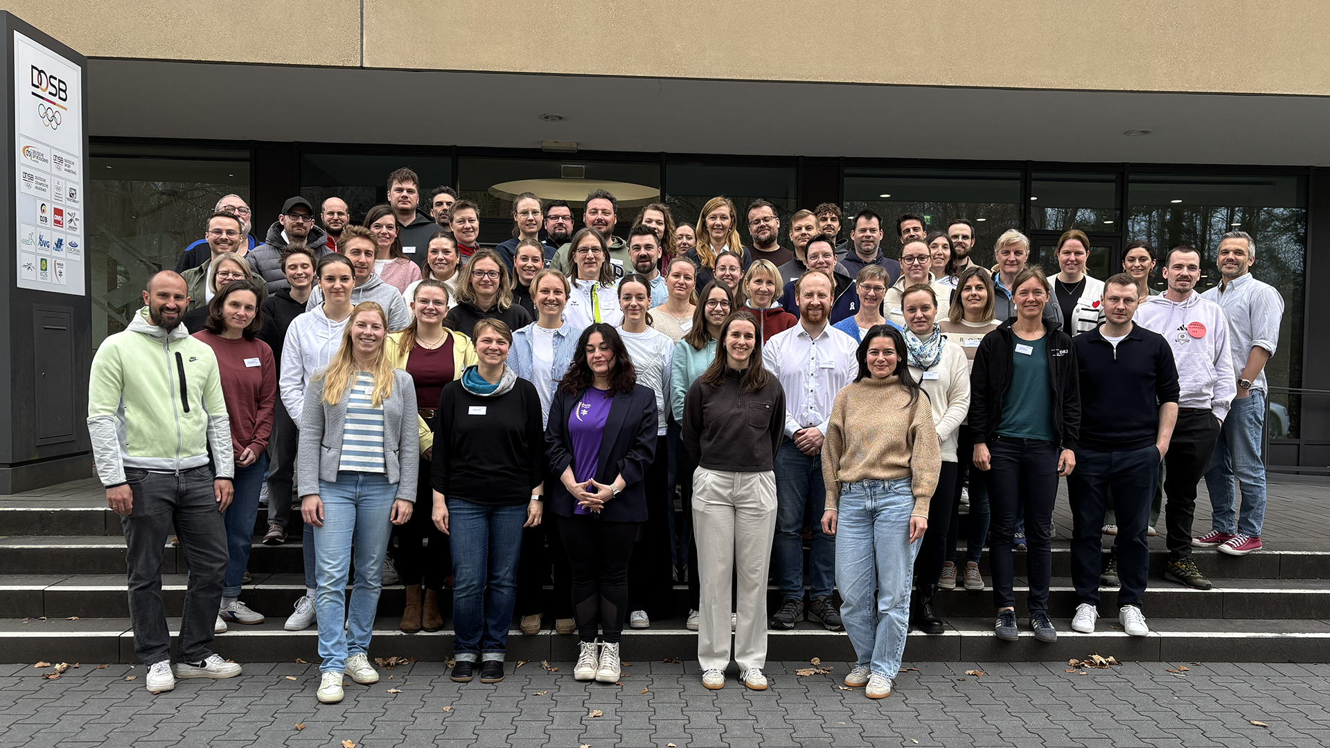 Gruppenfoto der Teilnehmenden beim Auftakt des Projekts NextLevelWir vor einem Gebäude, die gemeinsam auf den Stufen stehen.