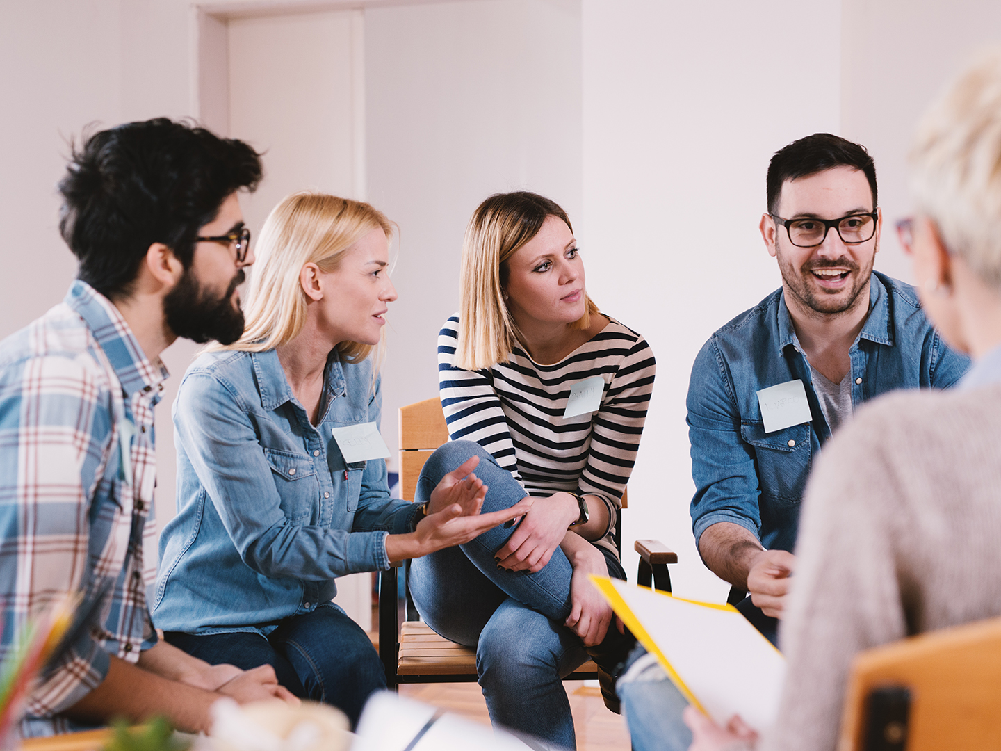 Eine Gruppe von fünf Personen sitzt in einem Raum und diskutiert. Sie wirken engagiert und aufmerksam, während sie sich gegenseitig ansprechen. Einige tragen Namensschilder. Der Raum ist hell gestaltet.