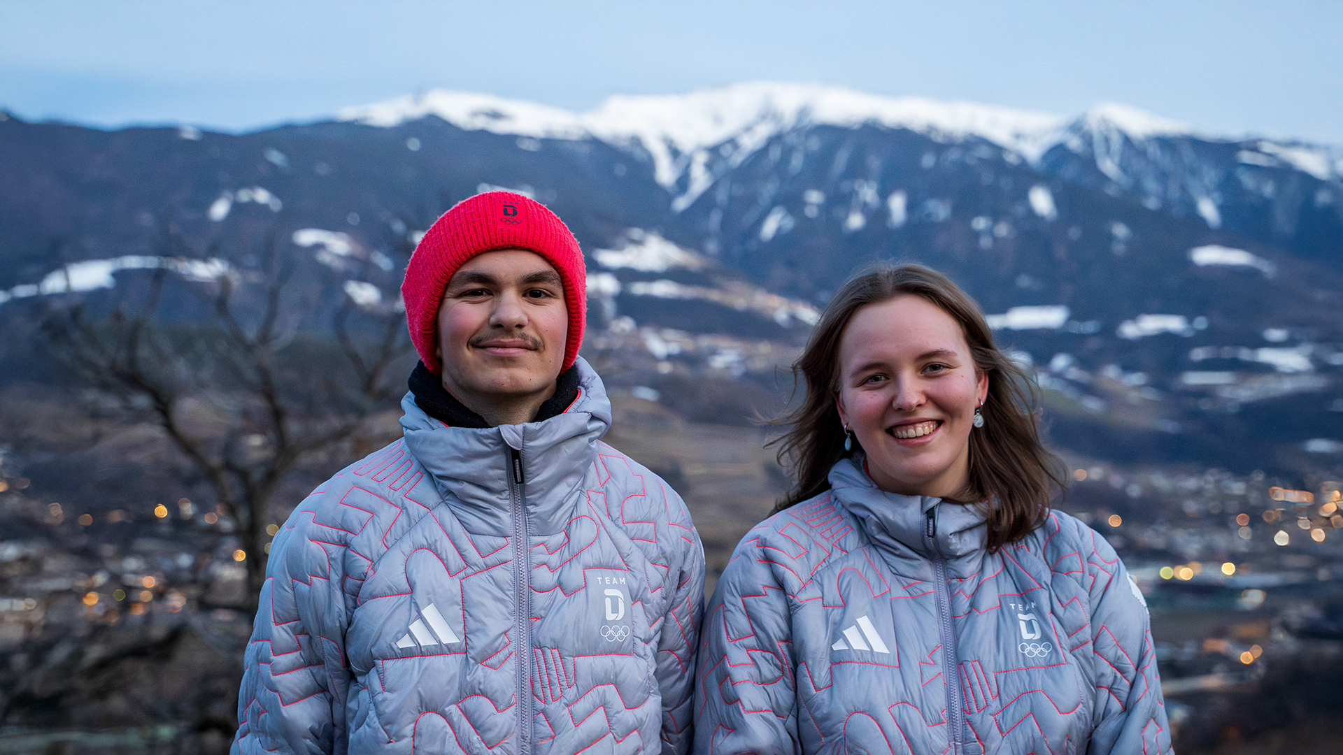 Isabelle Schneeweis und Leonard Schiller beim Olympischen Jugendlager in Cortina d’Ampezzo vor alpiner Berglandschaft.