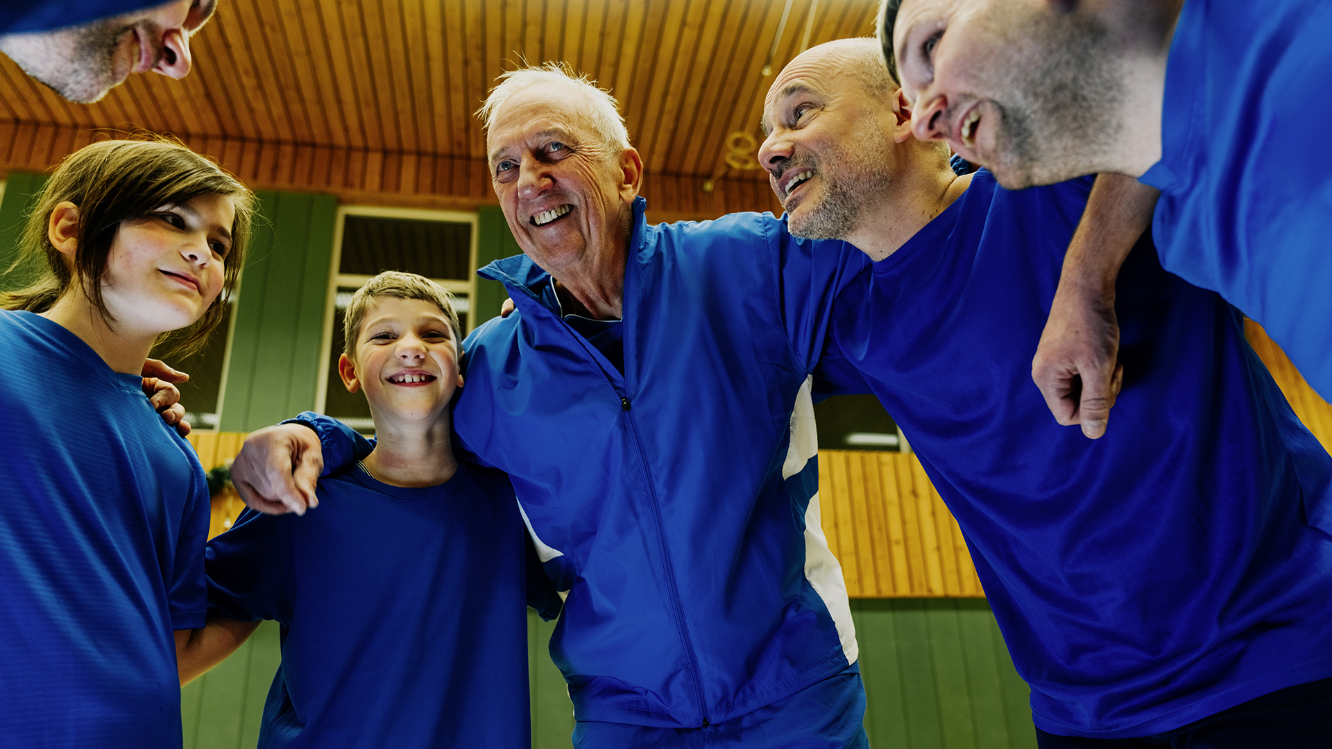 Sportmannschaft in blauen Trikots steht eng im Kreis in einer Sporthalle, legt die Arme umeinander und stimmt sich gemeinsam auf ein Spiel ein – Ausdruck von Teamgeist, Zusammenhalt und Fairplay im Vereinssport.