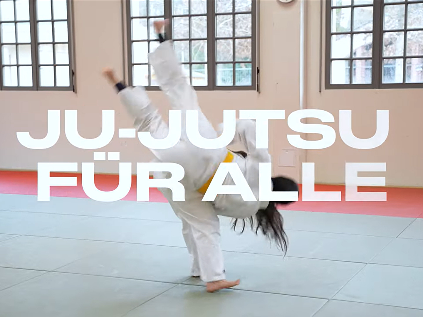Eine Person in einem weißen Ju-Jutsu-Anzug führt einen Kick aus. Im Vordergrund steht der Text "JU-JUTSU FÜR ALLE". Der Hintergrund zeigt einen Trainingsraum mit großen Fenstern und Matten auf dem Boden.
