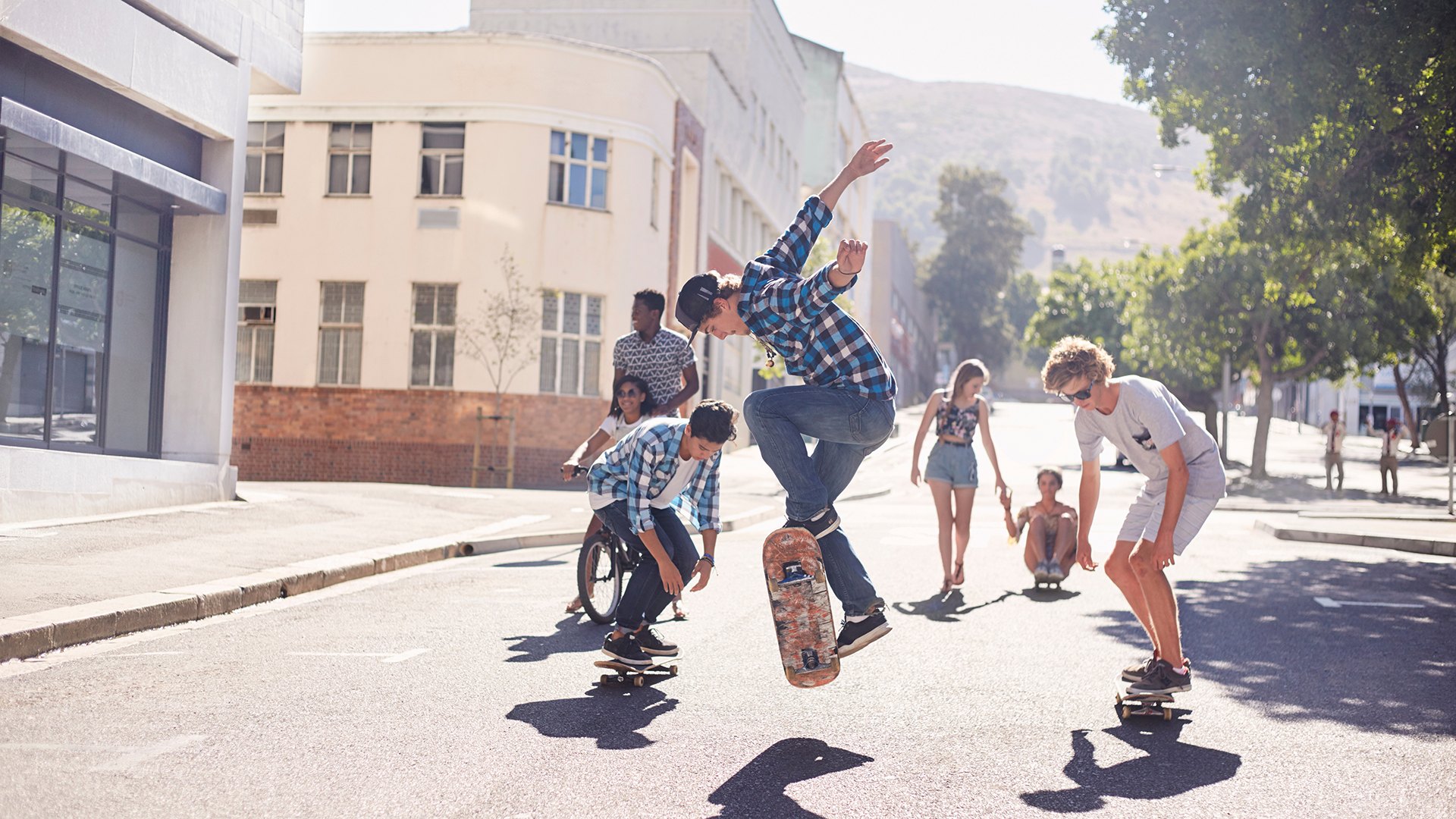 Jugendliche und junge Erwachsene fahren gemeinsam Skateboard auf einer Straße im urbanen Raum. Die Szene zeigt gemeinschaftliche Aktivität, Bewegung und Begegnung im öffentlichen Raum.