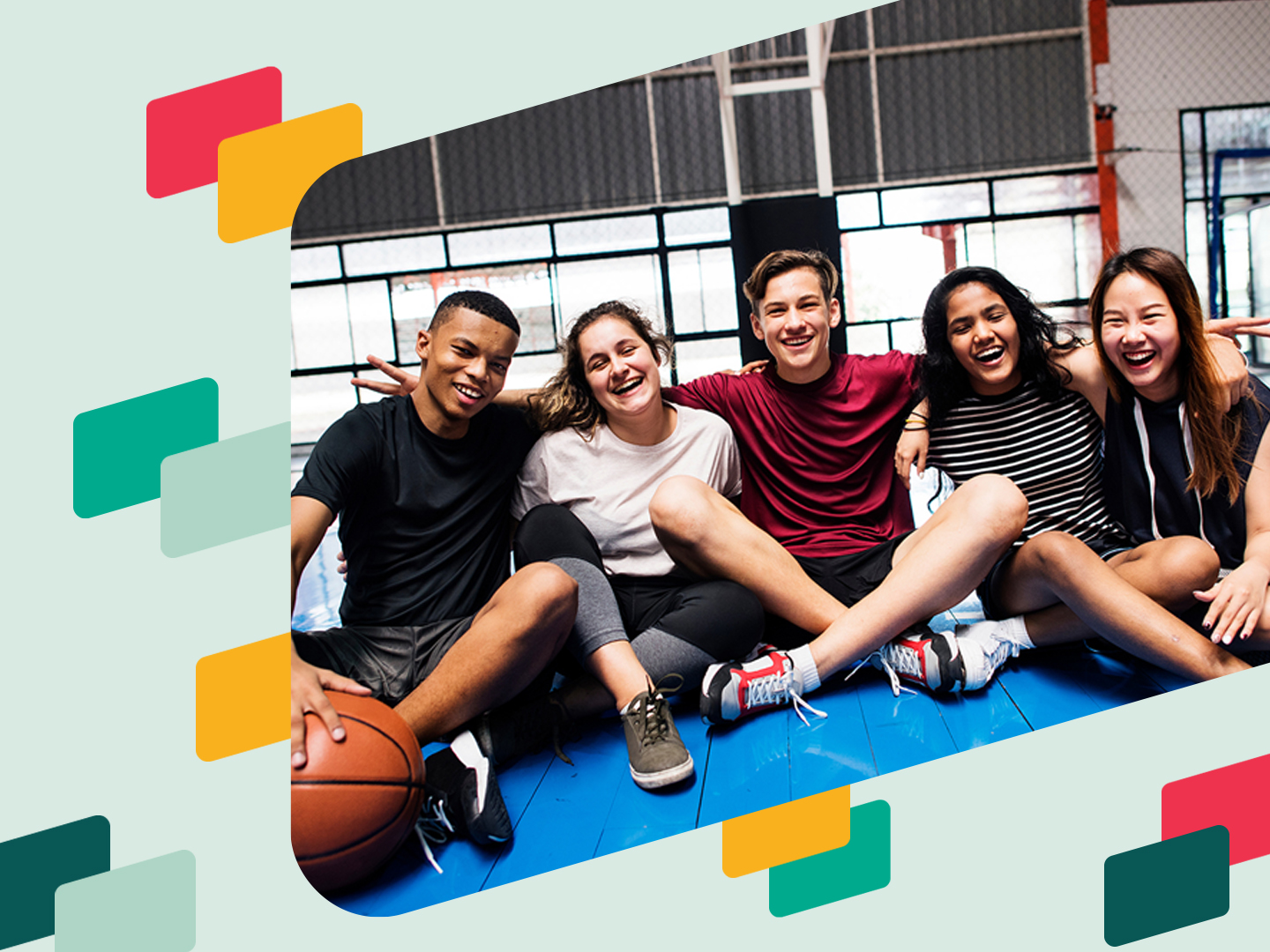Fünf junge Menschen sitzen auf dem Boden eines Basketballfeldes und lächeln in die Kamera. Sie tragen sportliche Kleidung und scheinen eine gute Zeit miteinander zu haben. Im Hintergrund sind Basketballkörbe und ein Netz sichtbar.