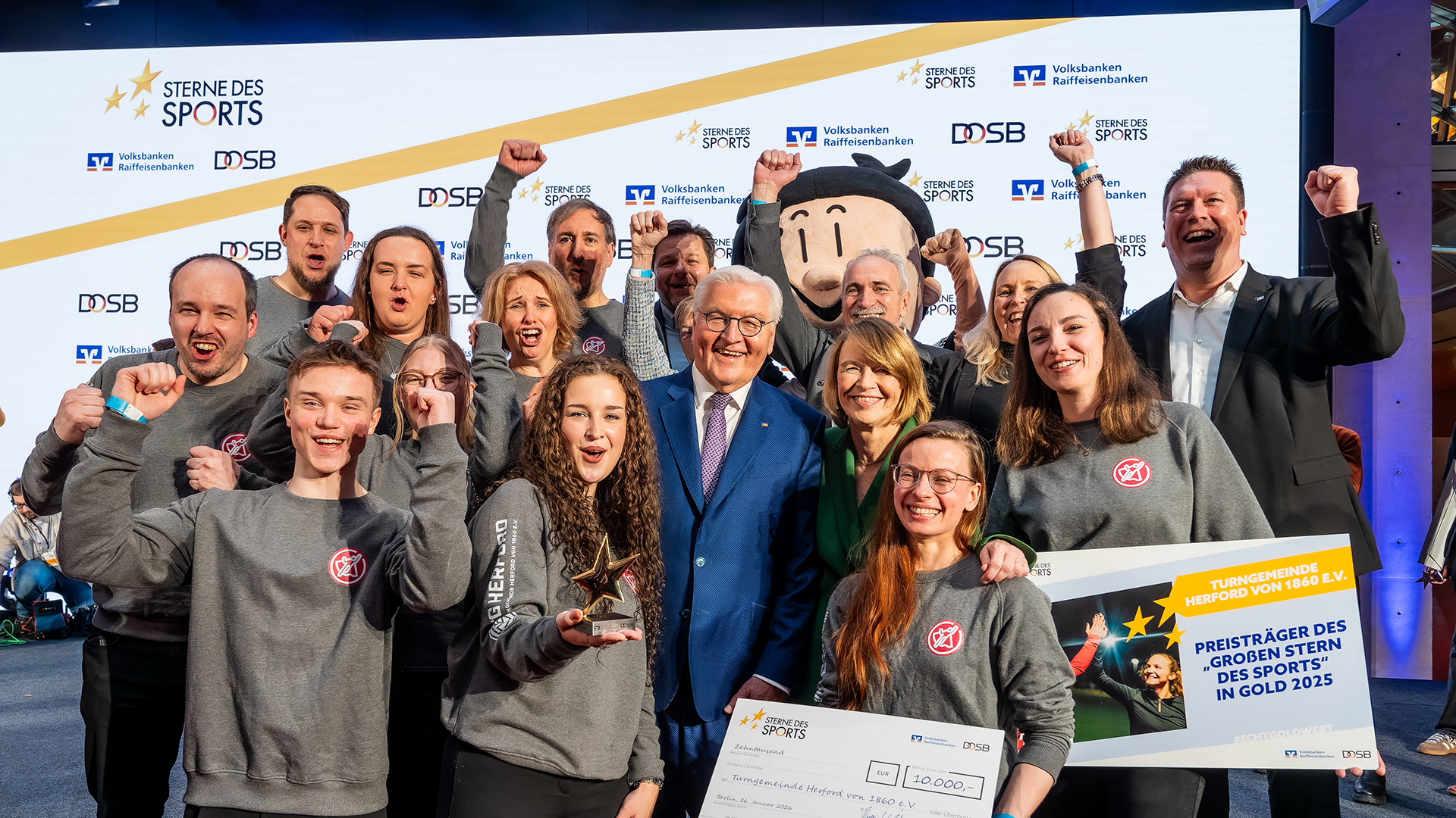 Gruppe eines Sportvereins bei der Preisverleihung „Sterne des Sports“ 2026 auf der Bühne, gemeinsam mit frank Walter Steinmeier und einem großen Siegercheck. Die ausgezeichneten Jugendlichen halten den Goldpreis stellvertretend für ihr Engagement im Kinder- und Jugendsport hoch.