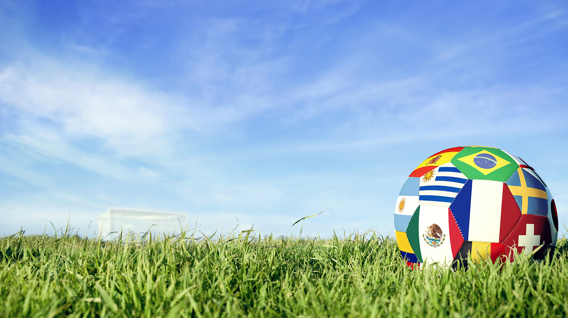 Fußball mit Flaggen verschiedener Länder liegt auf grünem Gras unter blauem Himmel, symbolisiert internationale Jugendarbeit und Veranstaltungen im 2. Halbjahr 2025