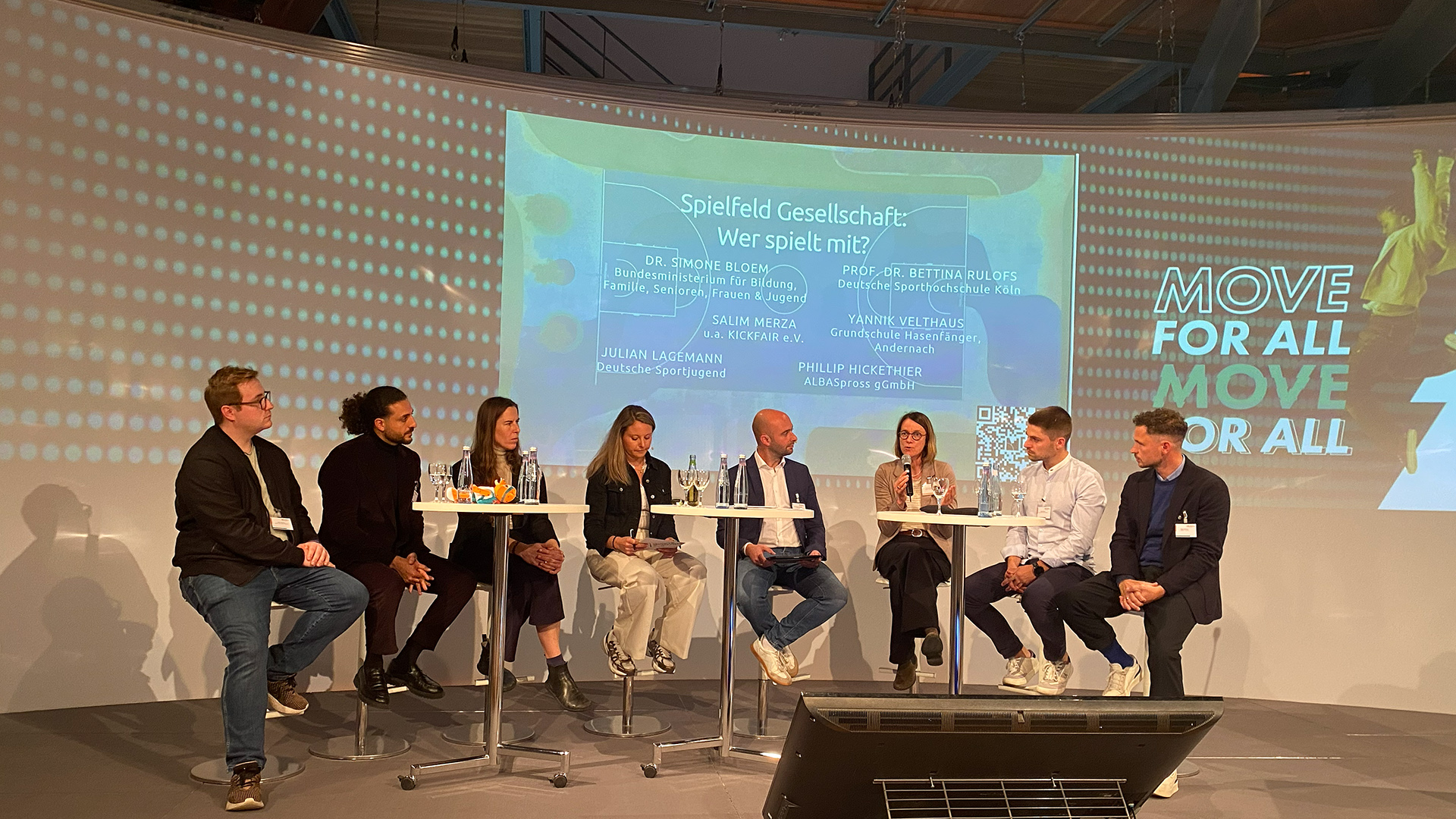 Podiumsdiskussion mit sieben Personen auf Bühne, im Hintergrund Projektion mit Text 'Spielfeld Gesellschaft: Wer spielt mit?' und MOVE-Forum 2025 Logo in Essen.