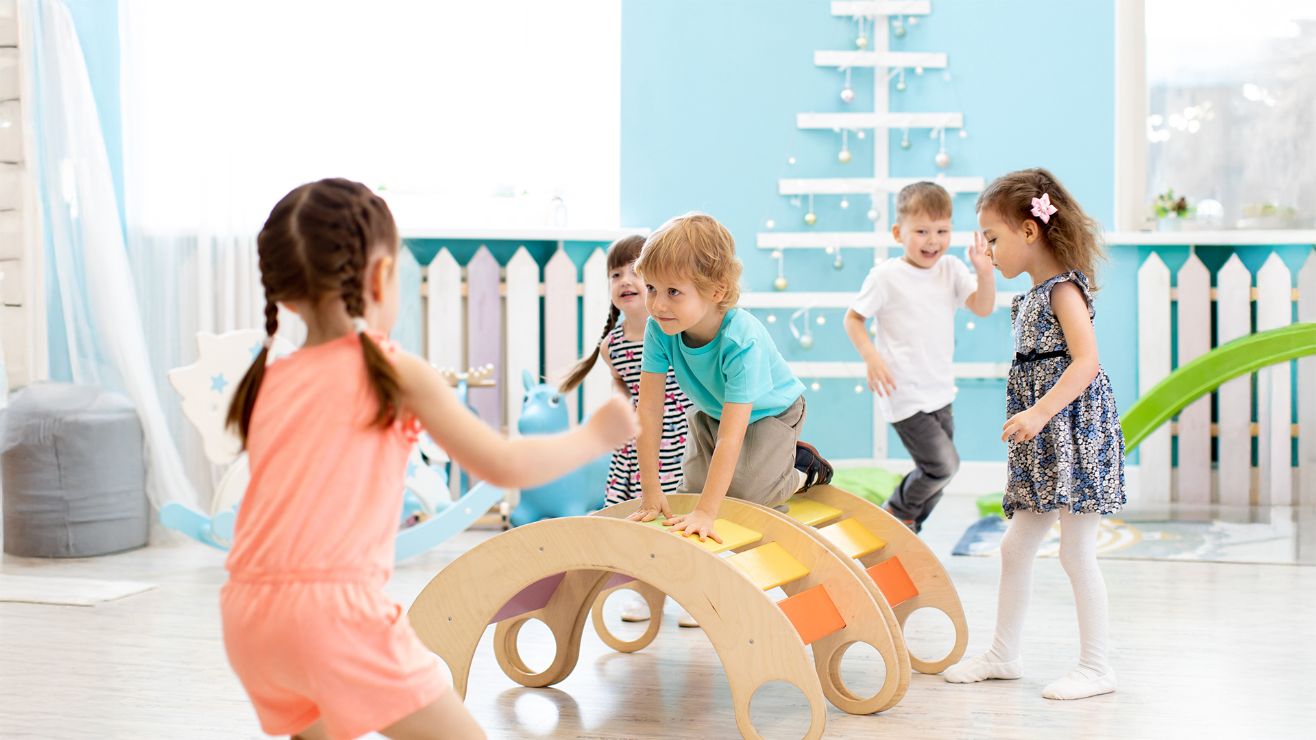 Kinder spielen in einer Kita mit einem Holz-Kletterbogen, der zur Bewegungsförderung dient
