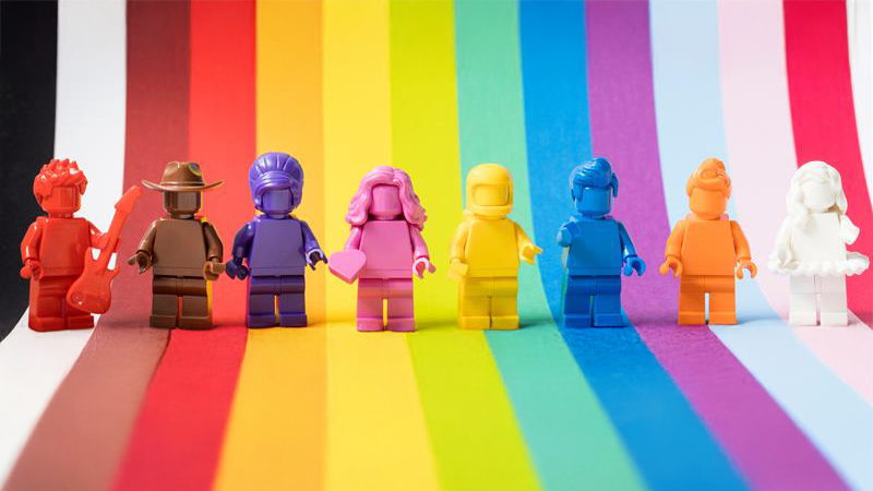 Acht bunte Lego-Figuren in Regenbogenfarben auf einem Regenbogenhintergrund, symbolisieren Vielfalt und queere Menschen im Sport bei SportPride 2025 am 28. Juni in München.