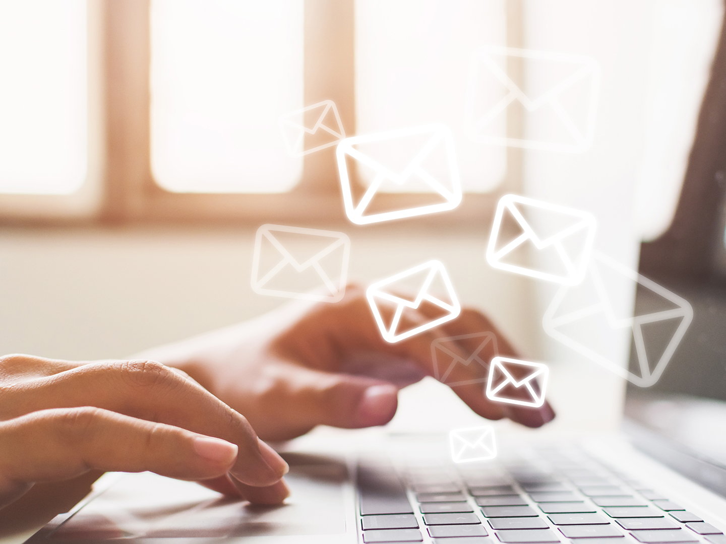 Eine Person tippt auf einer Laptop-Tastatur, während über dem Bildschirm stilisierte E-Mail-Symbole schweben. Das Bild vermittelt den Eindruck von Kommunikation und digitalem Austausch.