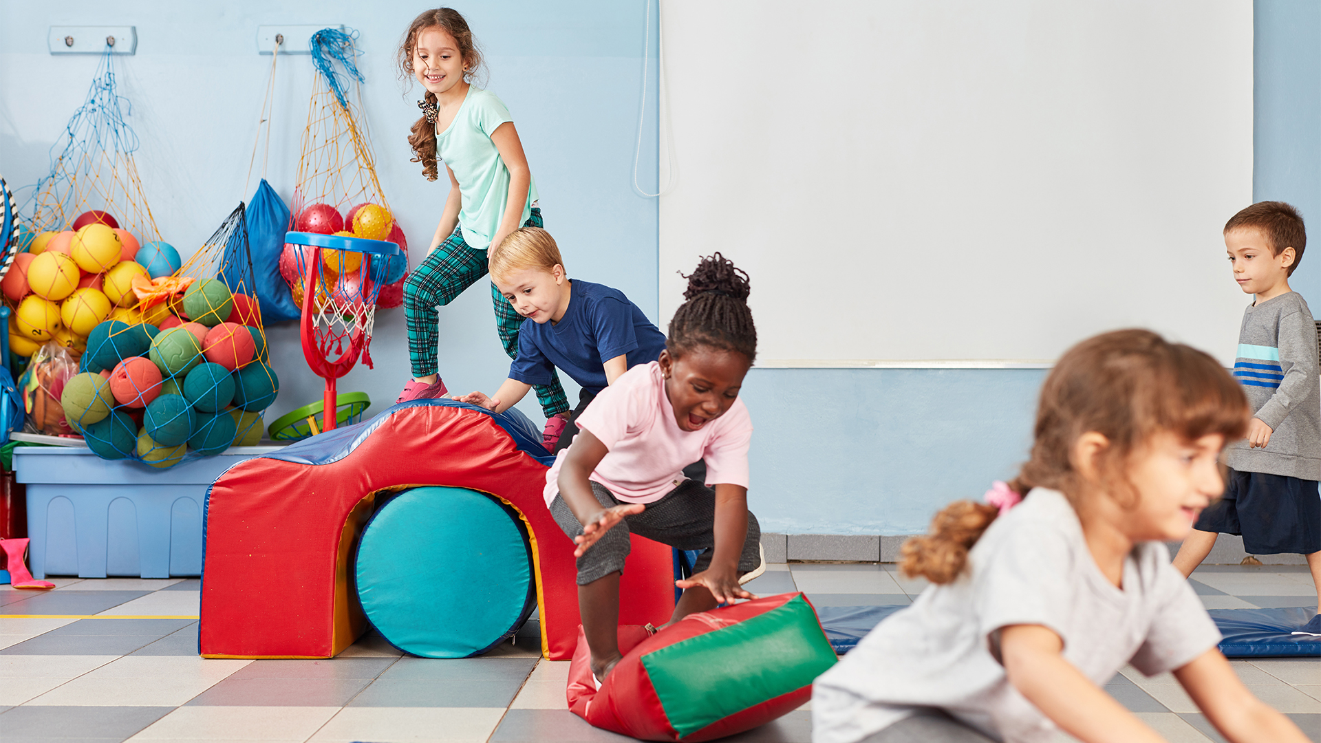 Kinder spielen in einer Sportini-Kita mit bunten Bällen und weichen Kletterelementen in einem hellen Raum