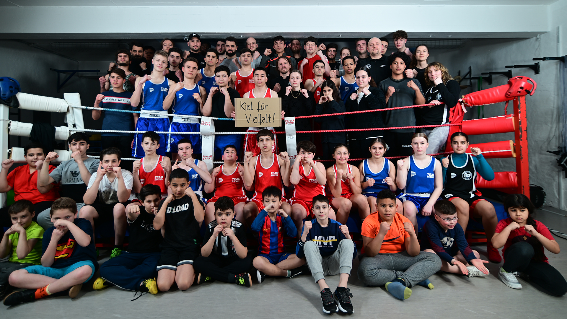 Gruppenfoto von Boxern des BSC Kiel in roten und blauen Trikots im Boxring, Gewinner des Vereinswettbewerbs '(M)ein Verein gegen Rassismus'