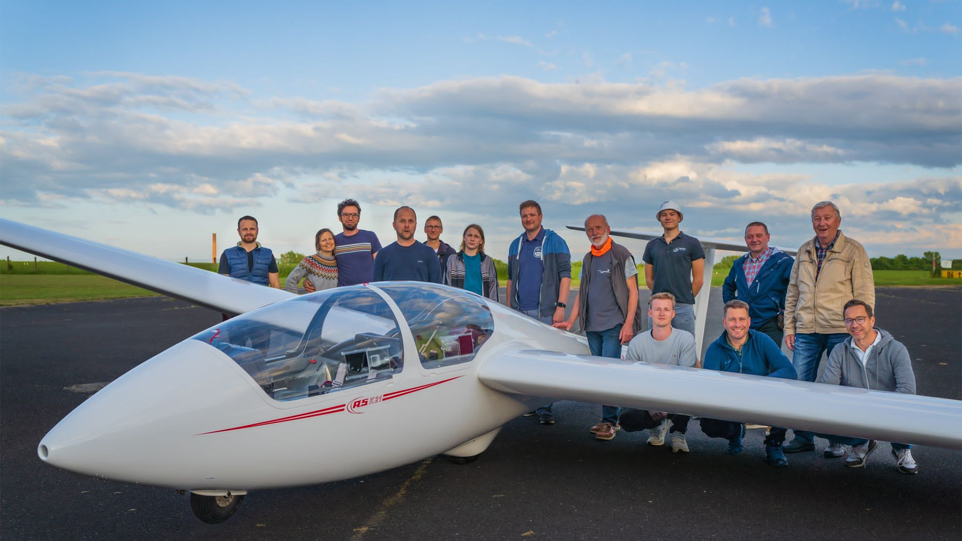 Mitglieder des Görlitzer Flugsportclubs posieren neben einem weißen Segelflugzeug auf dem Flugplatz, 2. Platz beim Vereinswettbewerb '(M)ein Verein gegen Rassismus' im Sport