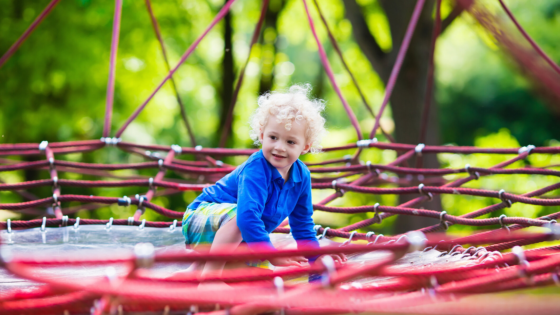 blond boy crawls on a red jumping net and has fun