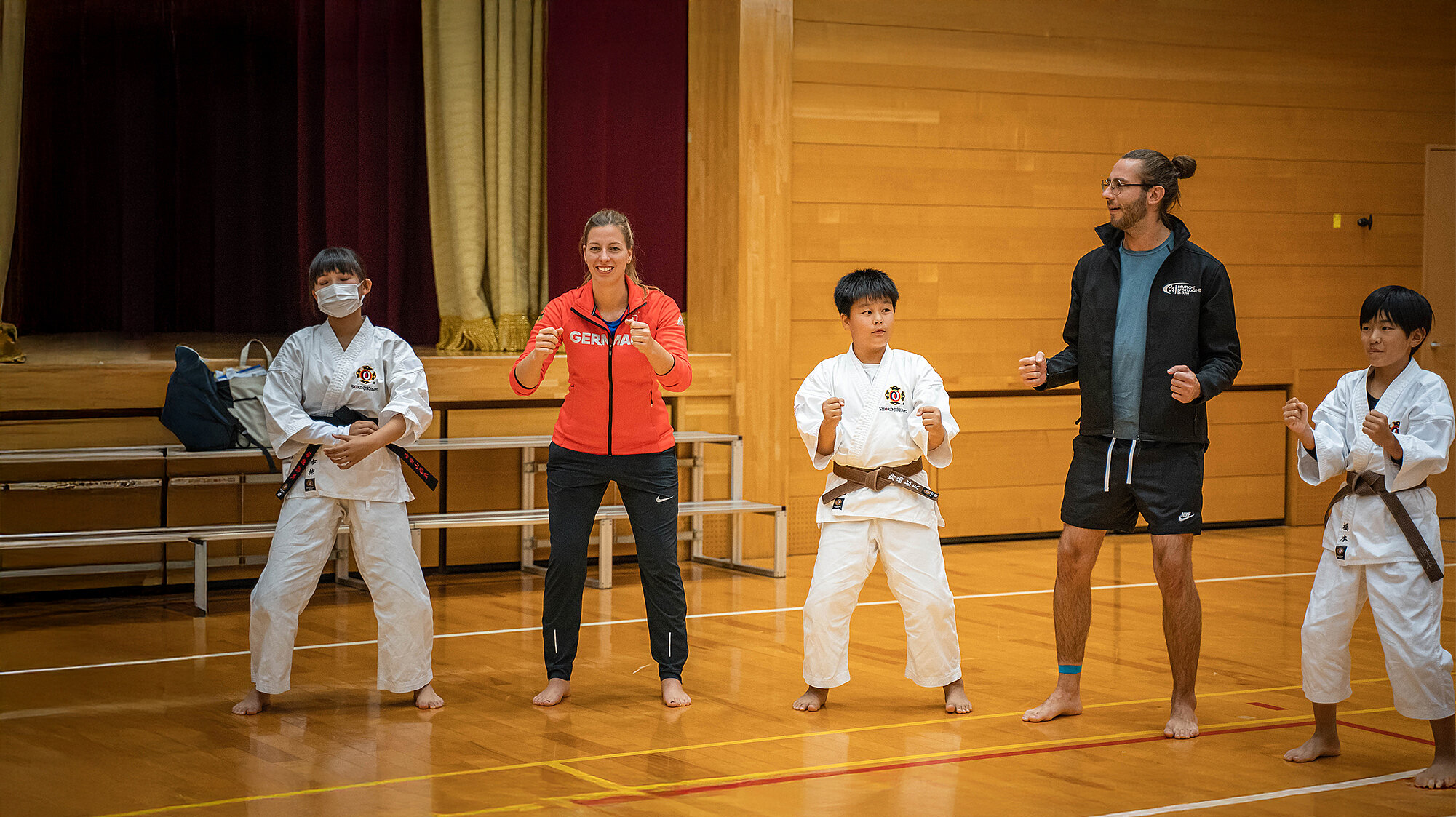 Fünf Personen in Sportkleidung und Karateanzügen stehen in einer Turnhalle in Kampfstellung beim Deutsch-japanischen Fachkräfteaustausch in Japan.