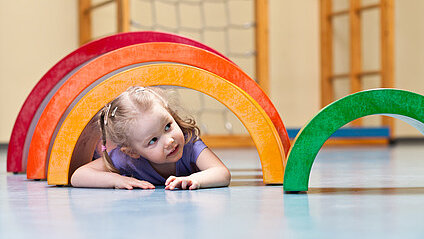 small, blonde girl under a wooden rainbow in a sports hall