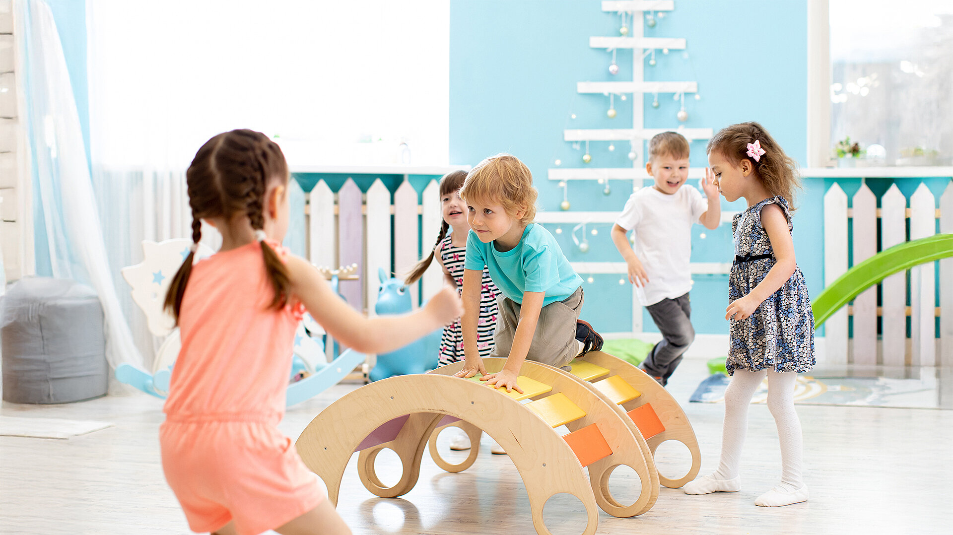 Kinder spielen in einer Kita mit einem Holz-Kletterbogen, der zur Bewegungsförderung dient