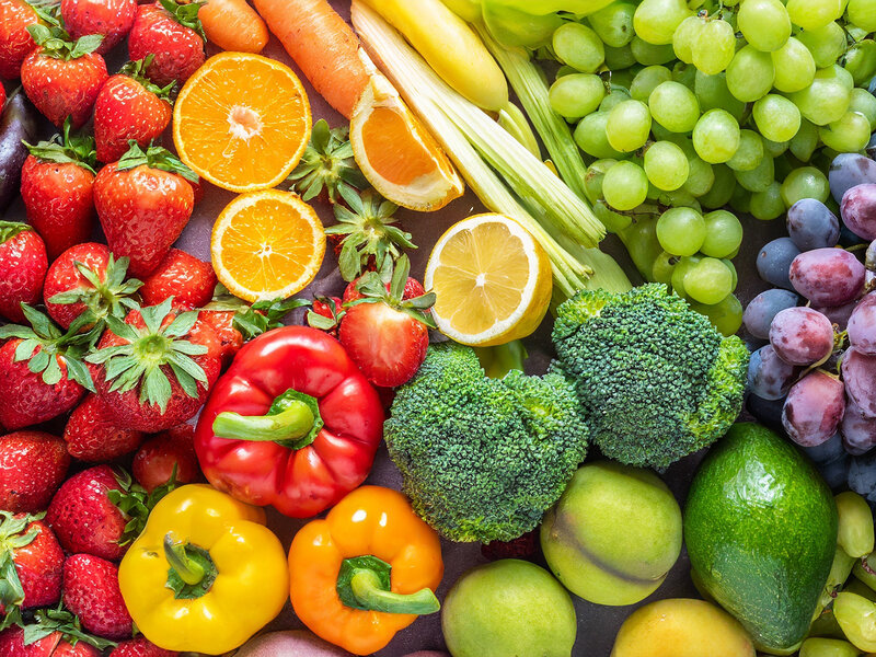 Verschiedene frische Obst- und Gemüsesorten wie Erdbeeren, Orangen, Trauben, Paprika und Brokkoli liegen nebeneinander.