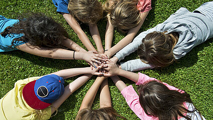 teenagers lie in a circle on the grass and put their hands together in friendship