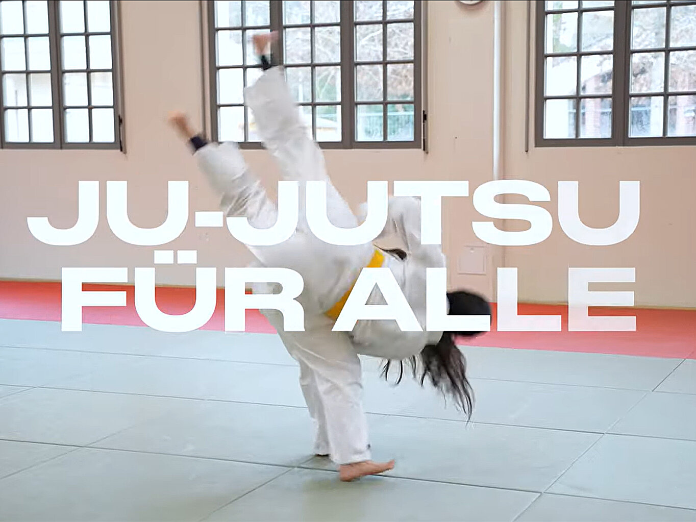Eine Person in einem weißen Ju-Jutsu-Anzug führt einen Kick aus. Im Vordergrund steht der Text "JU-JUTSU FÜR ALLE". Der Hintergrund zeigt einen Trainingsraum mit großen Fenstern und Matten auf dem Boden.