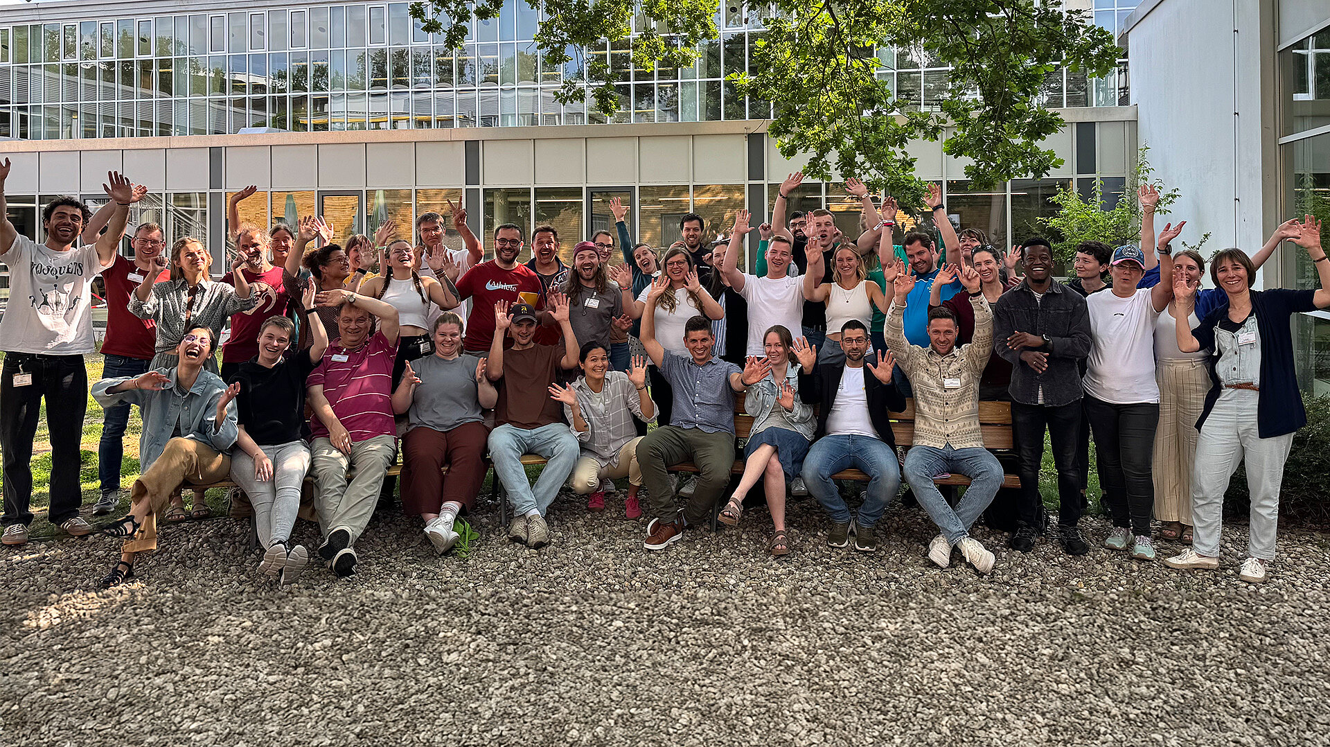 Gruppenfoto der Teilnehmenden der dsj-Fachtagung in Frankfurt zur internationalen Jugendarbeit im Sport, alle winken und lächeln vor einem modernen Gebäude.