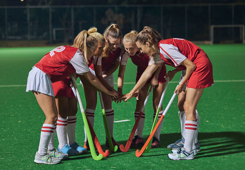 Mädchen und junge Frauen im Sport, die in roten Trikots auf einem Hockeyfeld stehen und ihre Hockeyschläger in der Mitte zusammenführen
