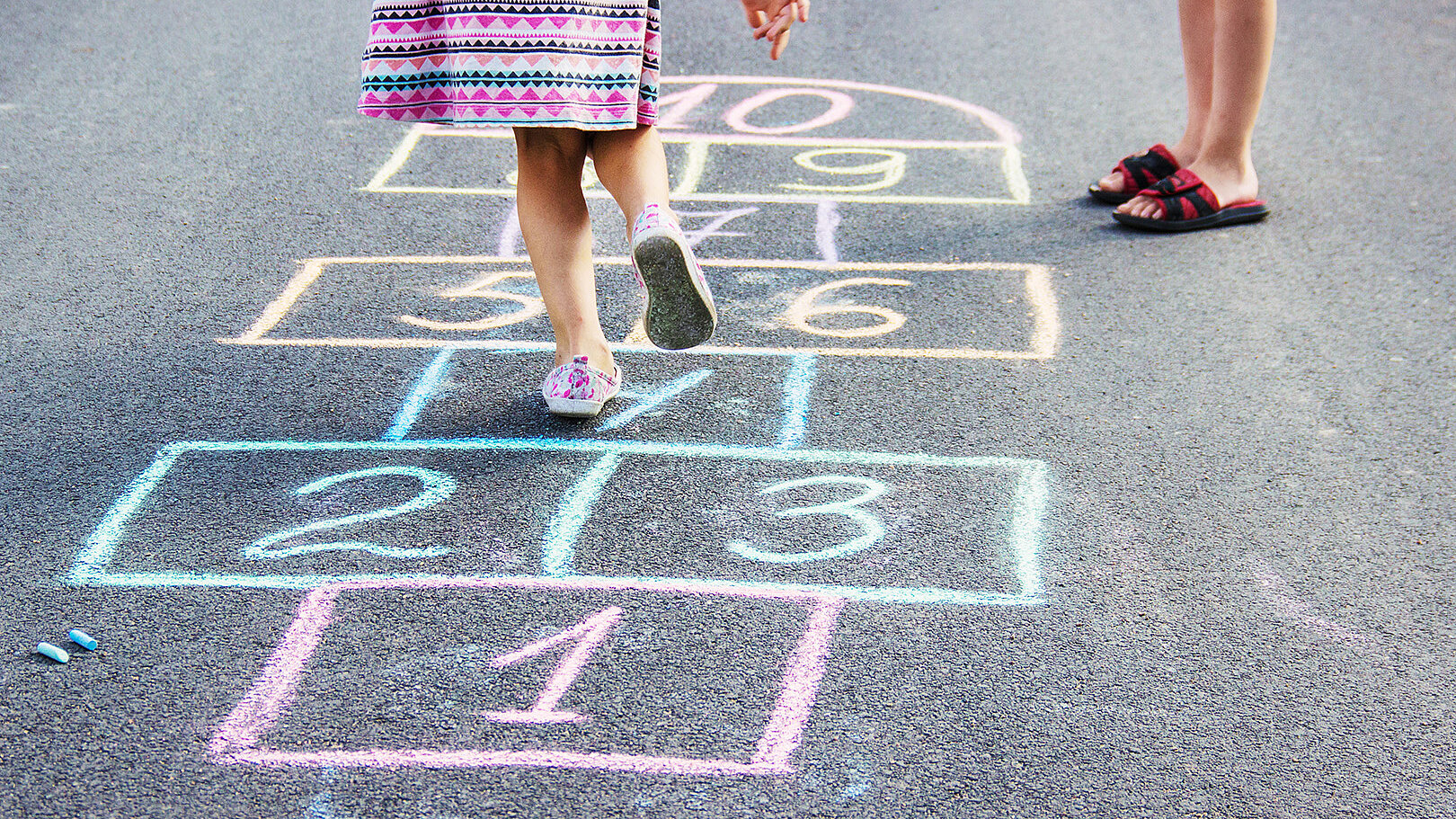 Kinder spielen Himmel und Hölle auf einem mit bunter Kreide gezeichneten Spielfeld auf Asphalt, Kooperation mit Kitas und Ganztagsschulen