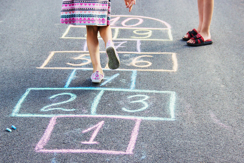 Kinder spielen Himmel und Hölle auf einem mit bunter Kreide gezeichneten Spielfeld auf Asphalt, Kooperation mit Kitas und Ganztagsschulen