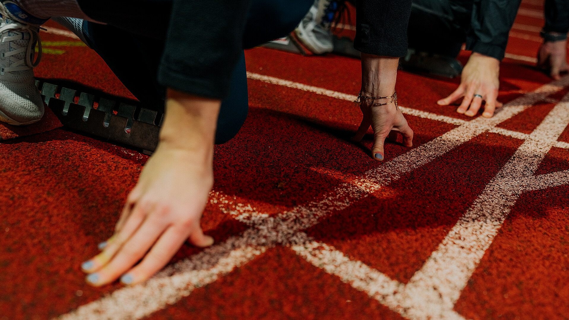 Athletinnen in Startposition auf roter Laufbahn mit weißen Linien, bereit für ein Rennen. FAQ: Rechtssicher positionieren