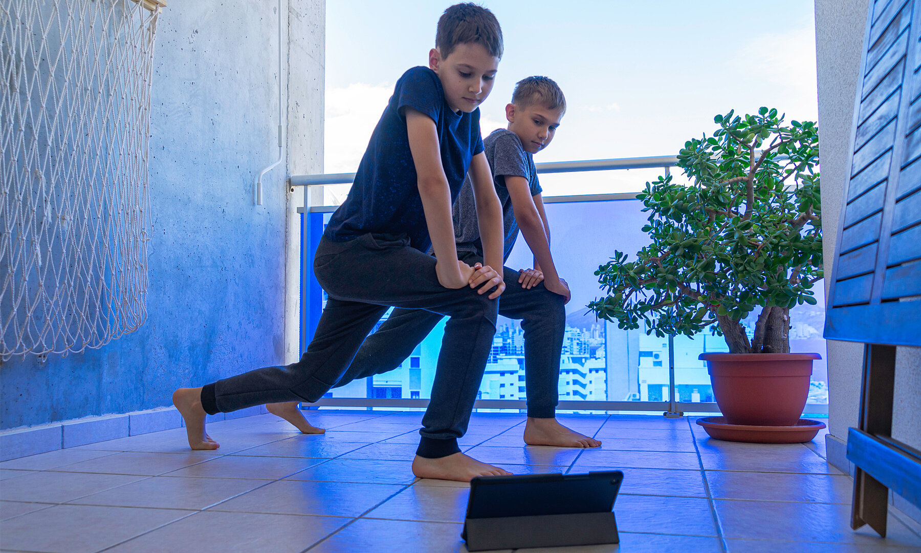Boy with laptop computer doing sport exercises on balcony. Sport, healhty lifestyle, active leisure at home 